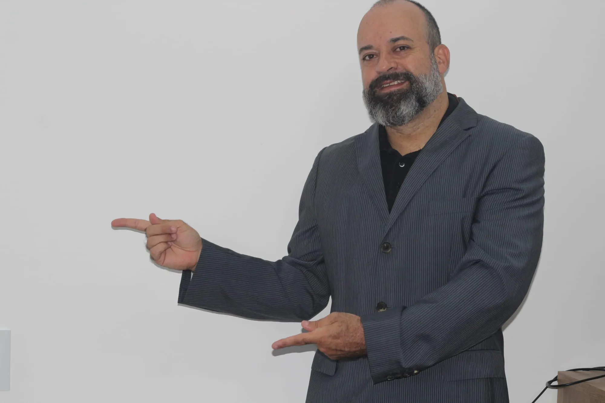 Alexandre Silva, consultor de SEO, de blazer, sorrindo e apontando para o lado