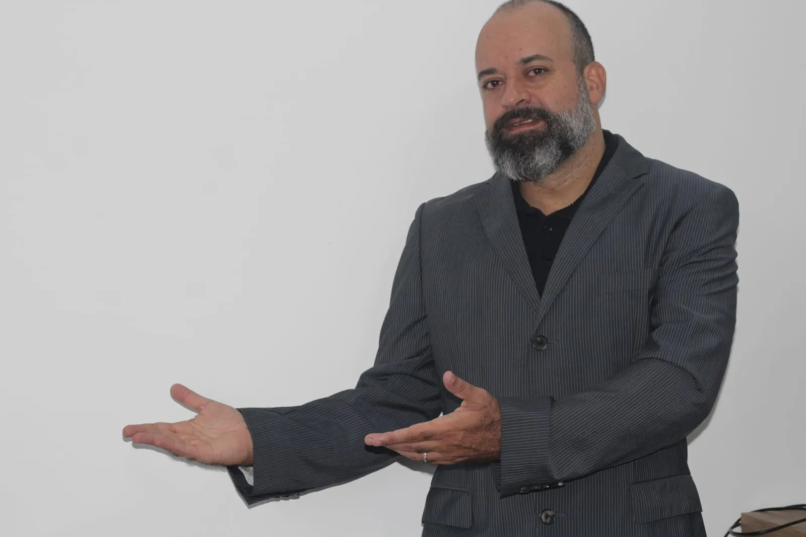 Alexandre Silva, consultor de SEO, de blazer, com as mãos abertas apresentando