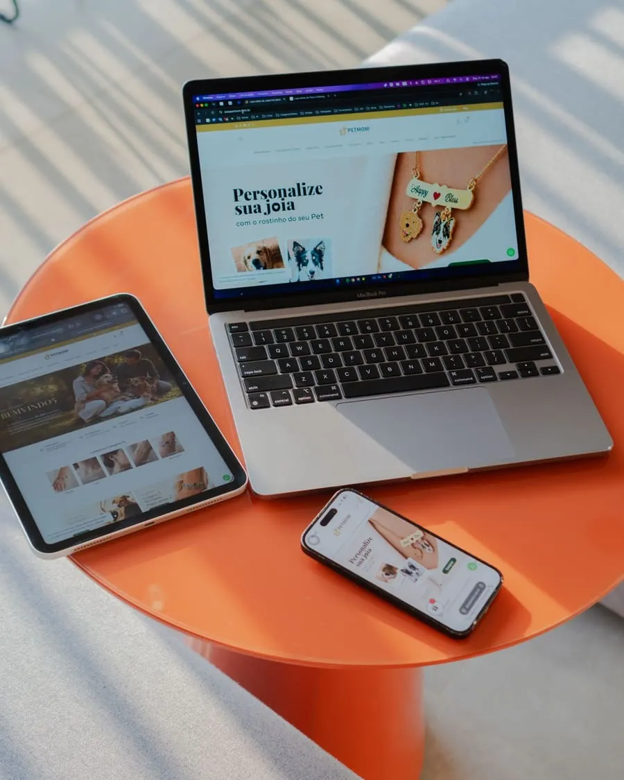 Notebook, tablet e celular mostrando páginas sobre uma mesa laranja