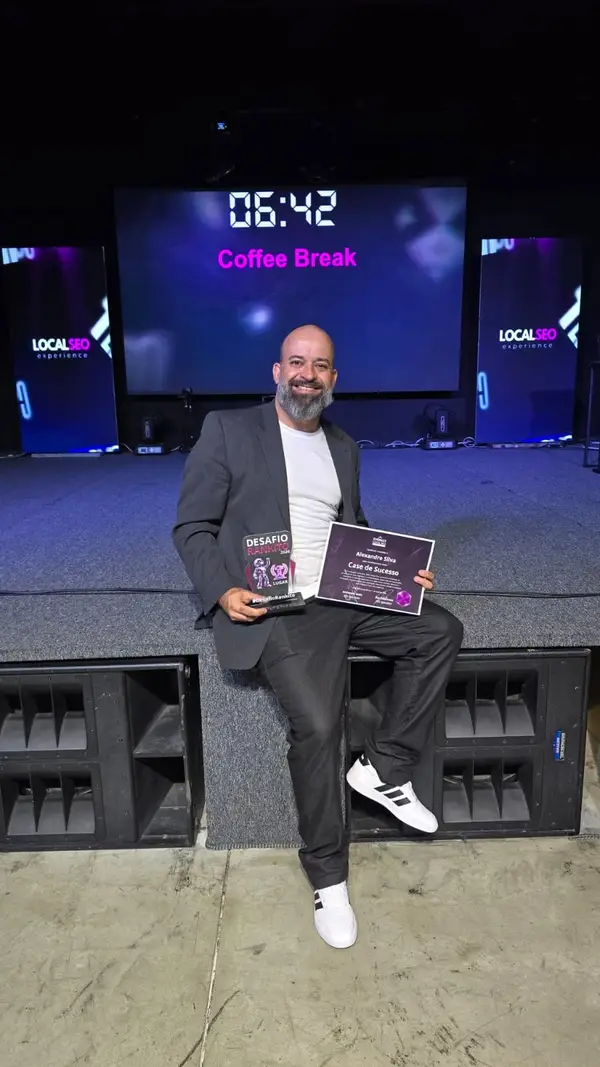 Alexandre Silva no palco da Formação Consultor SEO Local, em Mogi das Cruzes, segurando o certificado de Case de Sucesso