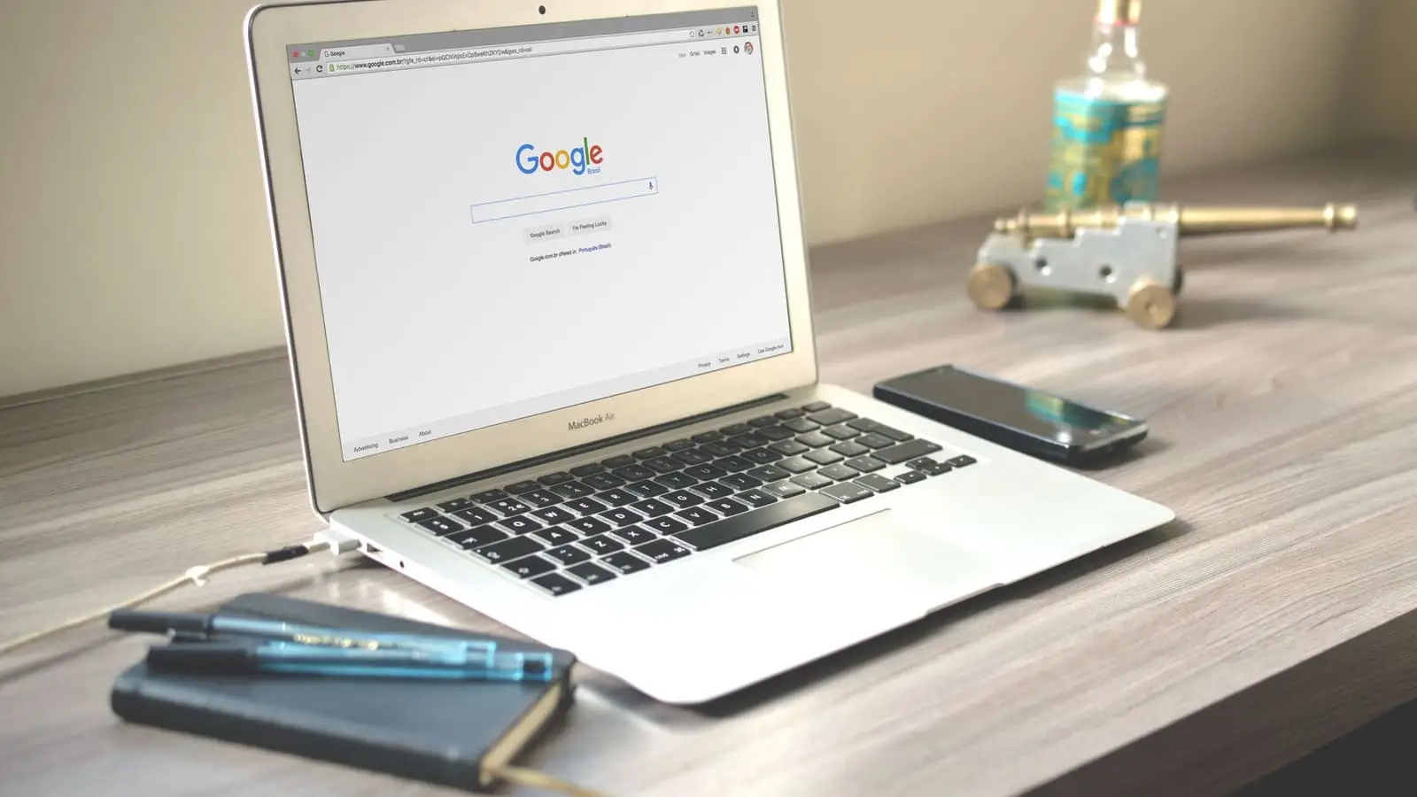 Notebook aberto na página de pesquisa do Google, ao lado de um celular e um caderno, sobre uma mesa